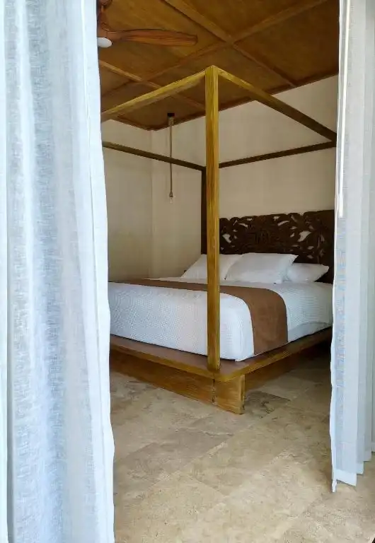 Cama bajo dosel, tras una cortina blanca.