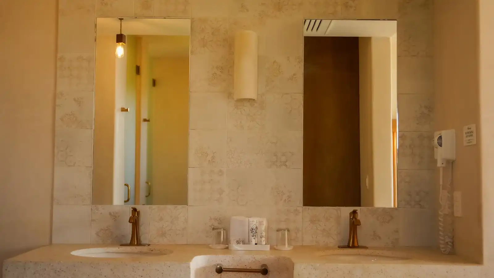 Doble lavabo de piedra con dos espejos y apliques de pared.