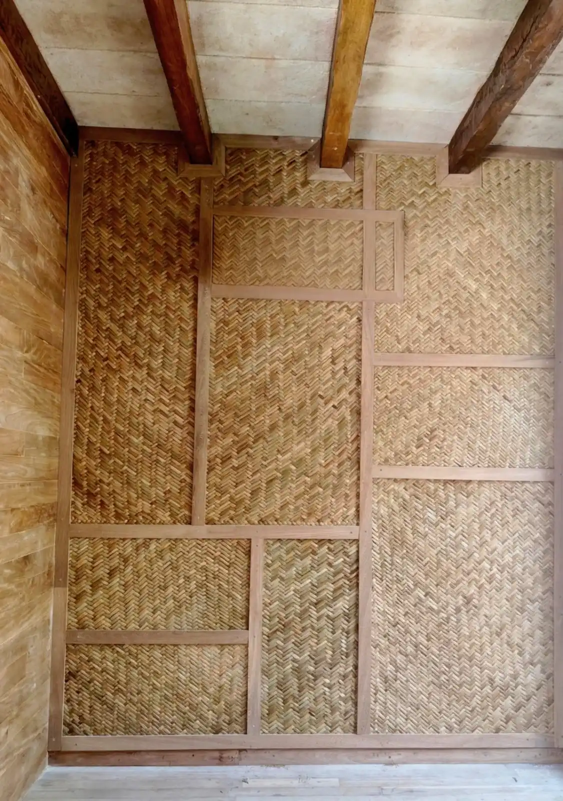 A wall of palm woven in a herringbone pattern, between wooden beams.