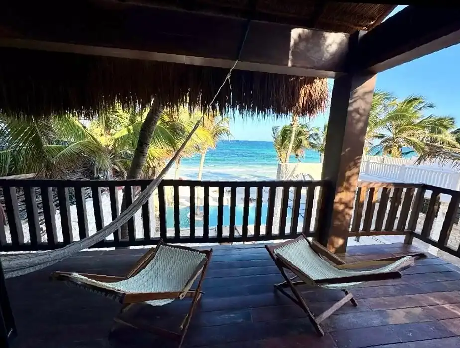 Two woven loungers on a palm-thatched terrace, looking out to the palm trees and the sea.