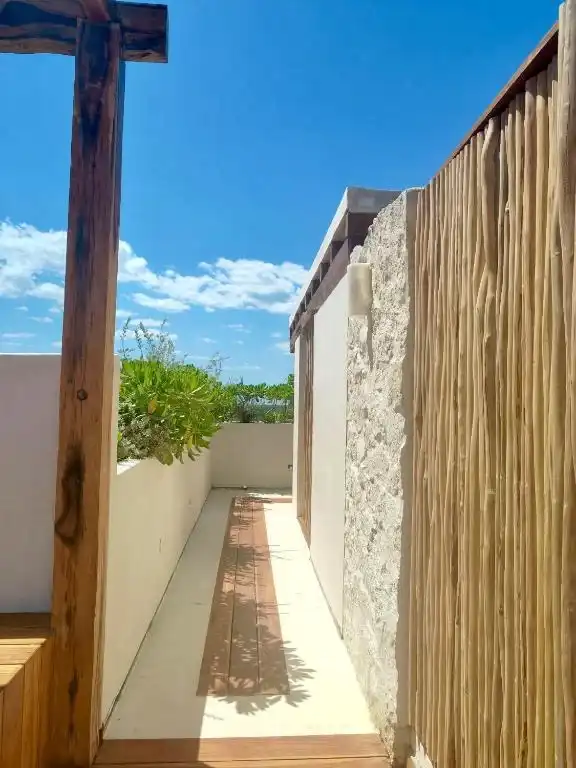 A narrow passage between a stone wall and a bamboo fence.