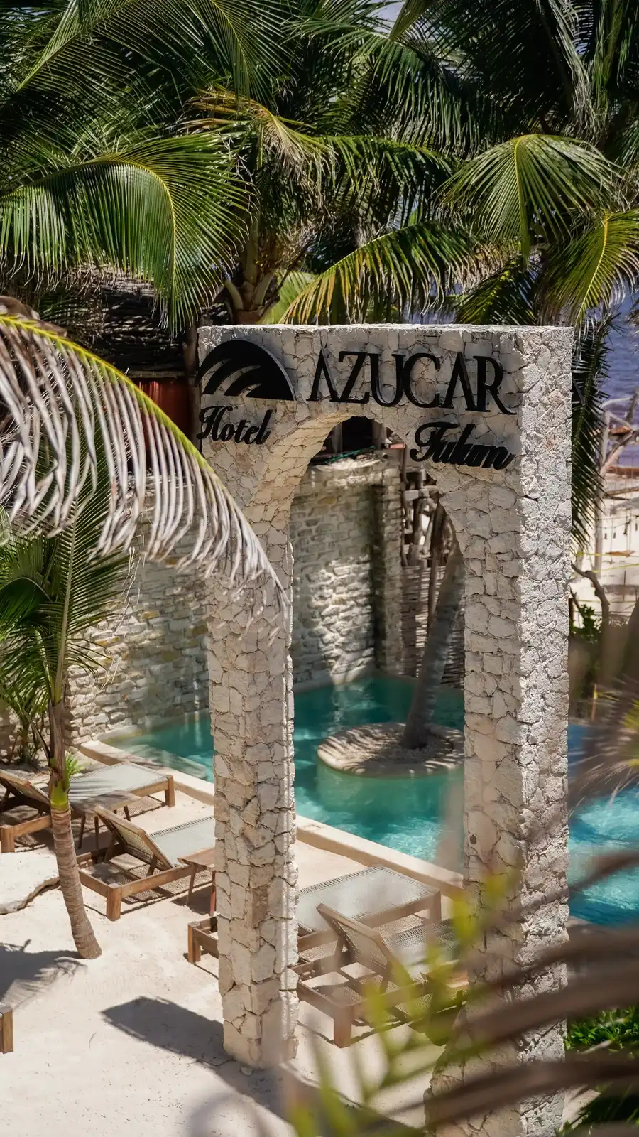 Arco de piedra con el rótulo del hotel y la alberca con su islita de palmera