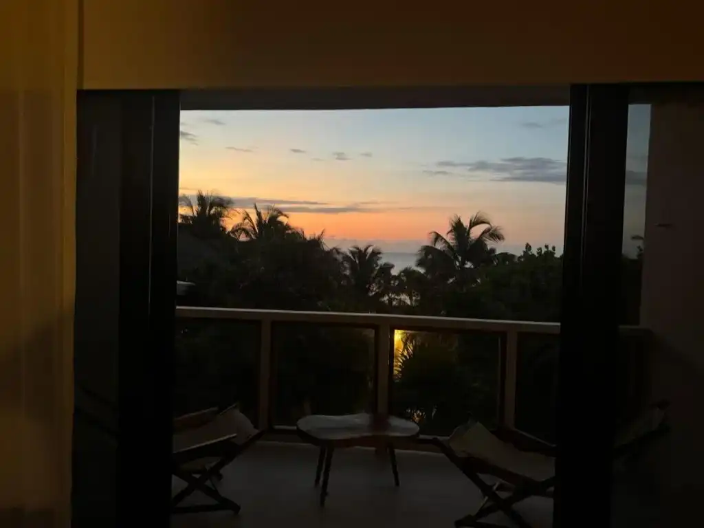 The balcony at sunset from inside the room, with two chairs.