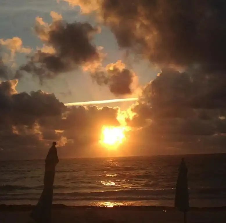 A cloudy sunset over the sea, the sun low on the horizon.