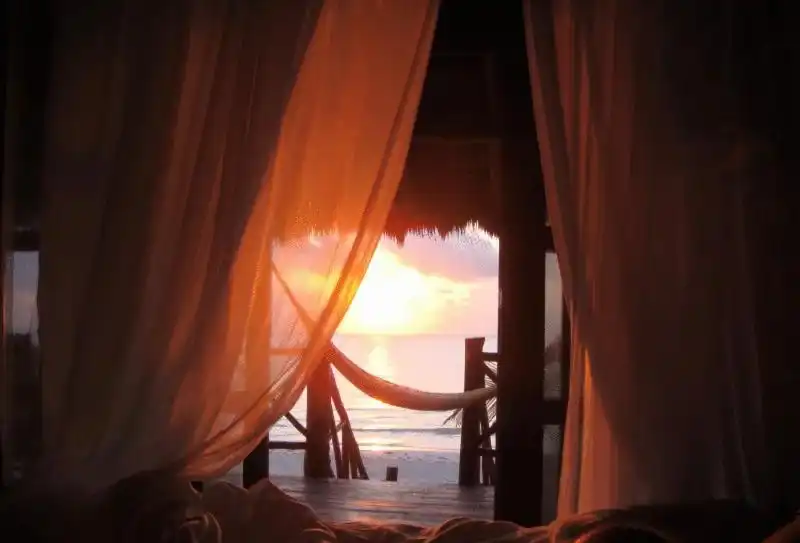 Curtains open onto the sunset, with the sea beyond.