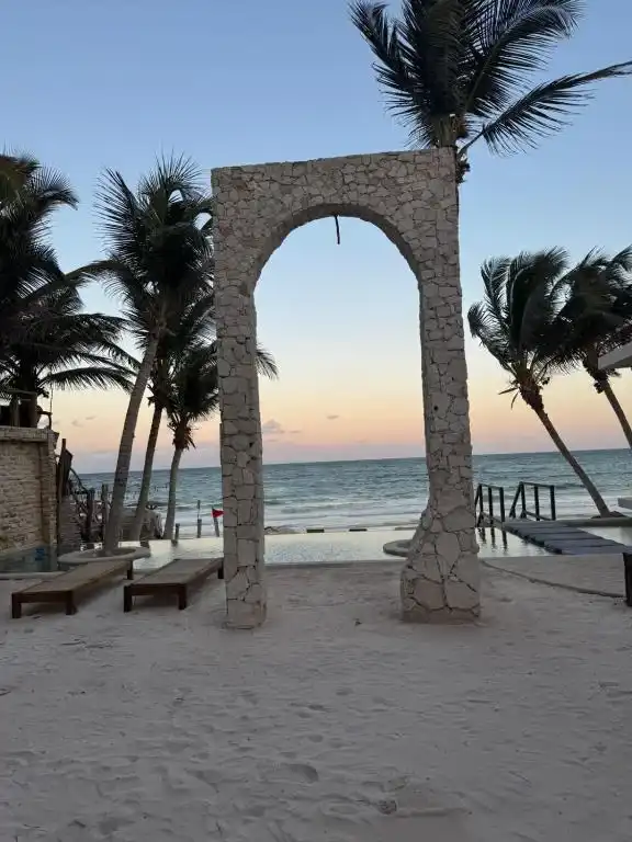 A stone arch on the beach between the palms, at sunset.