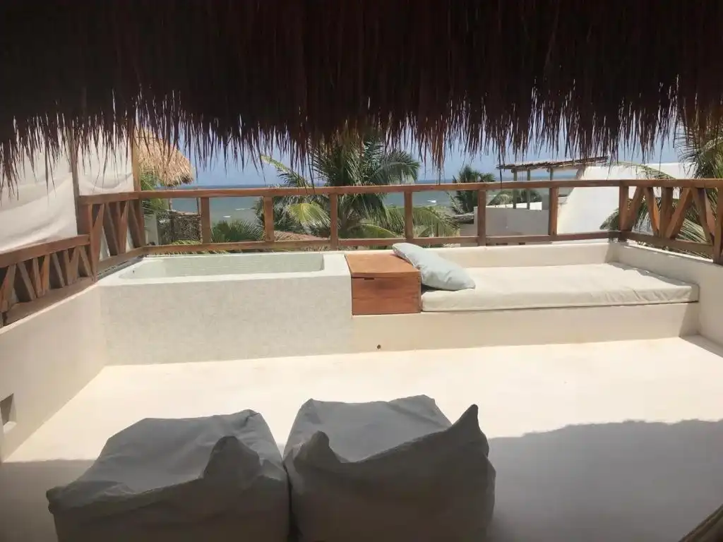 A rooftop terrace with a white daybed and cushions, under the palm eaves.