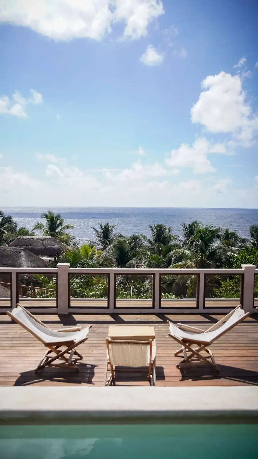 Wooden loungers beside the rooftop pool edge, with the palm trees and the sea behind.