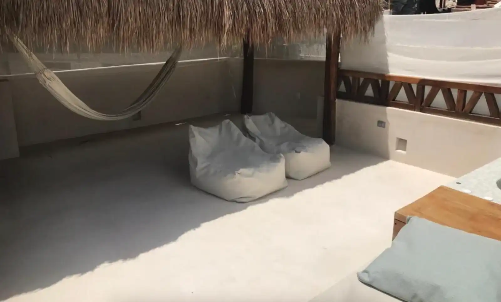A palm-roofed corner with a hammock, two bean bags and a low wooden table.