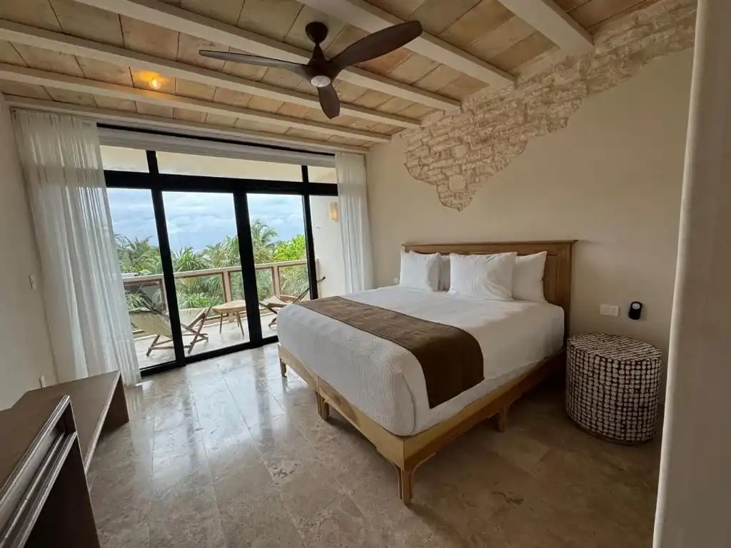 A room with a bed, a ceiling fan and a window wall onto the balcony.