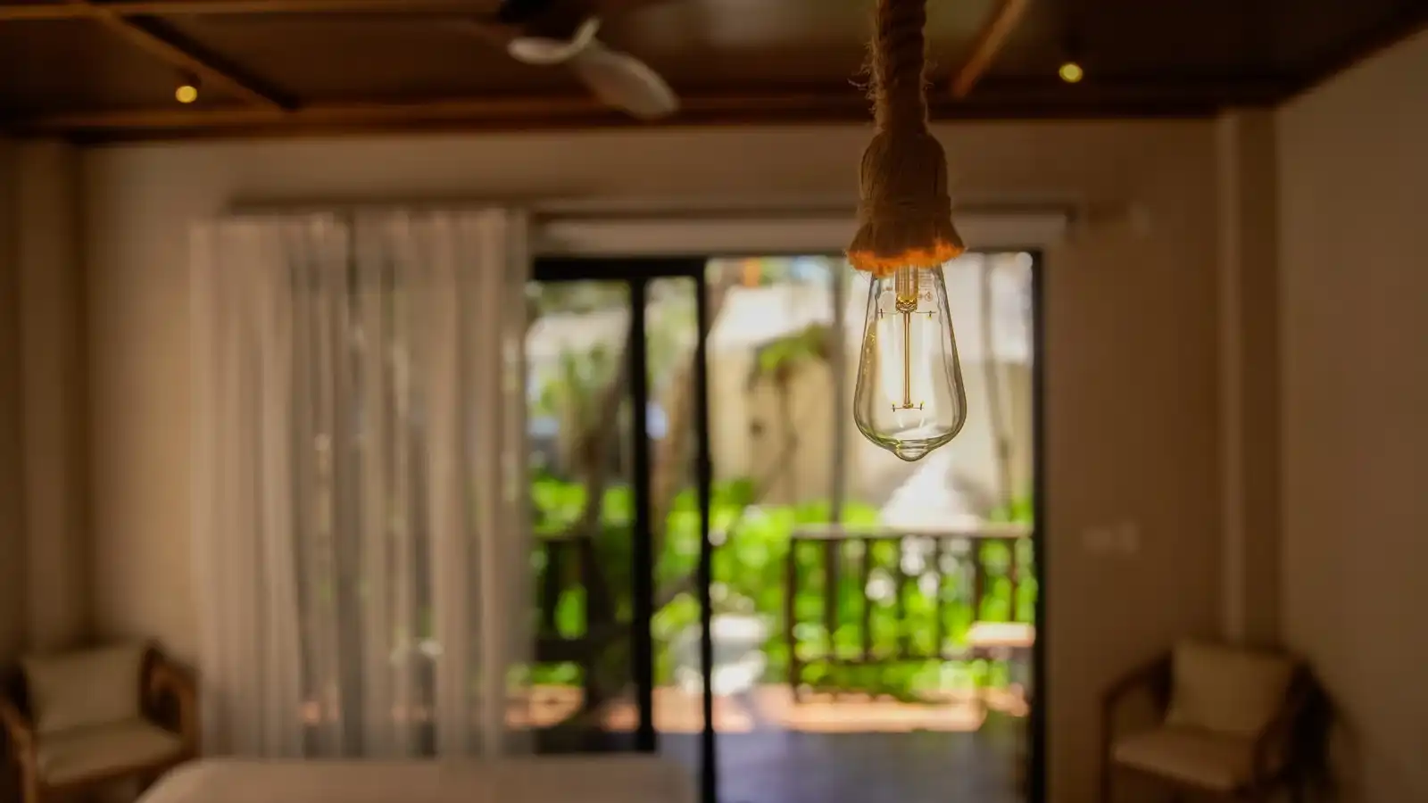 A dim interior with a hanging lamp, opening onto a terrace with armchairs.