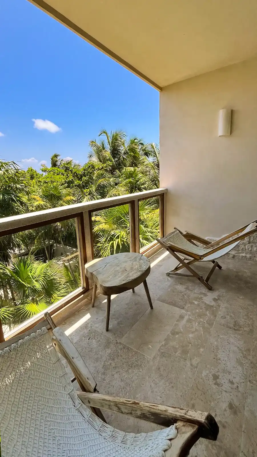 A balcony with a hammock and a wooden chair, greenery beyond the railing.