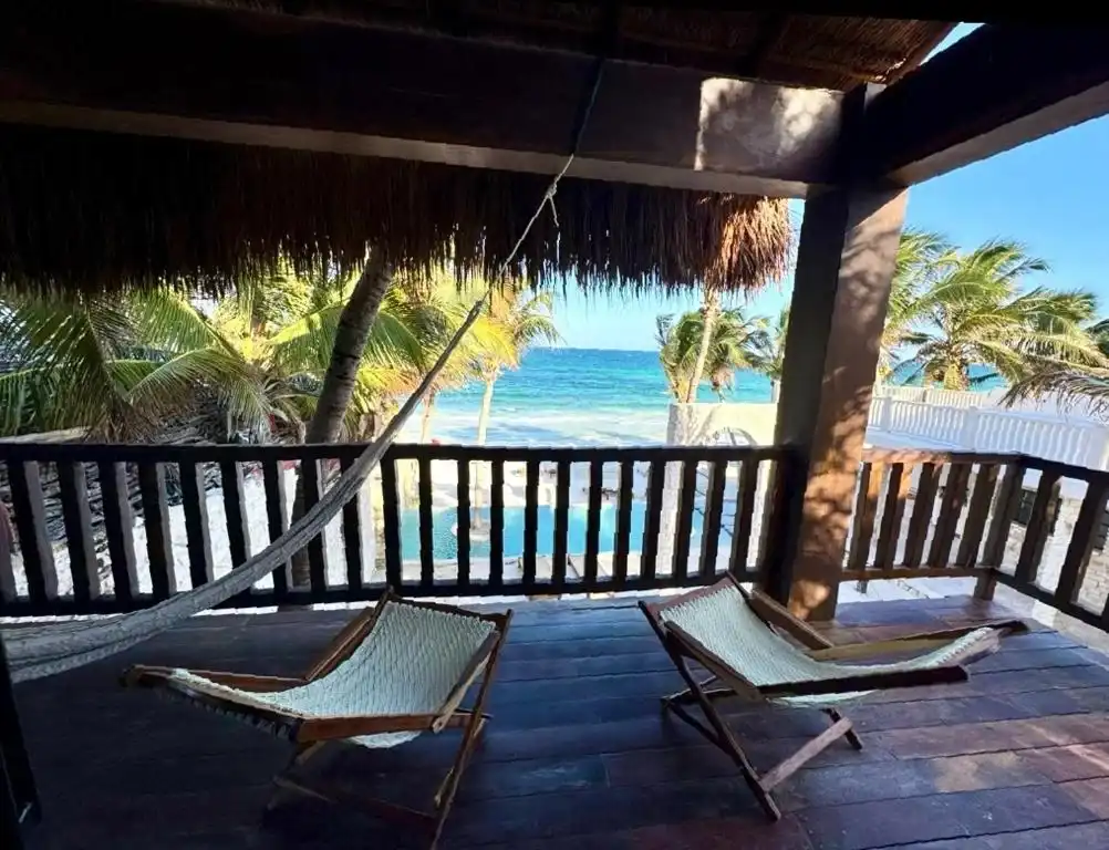 A palm-thatched terrace with two folding chairs, facing the sea.