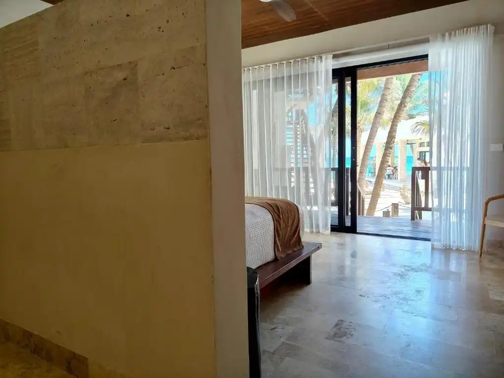 A room with the window wall open onto the balcony and the sea.