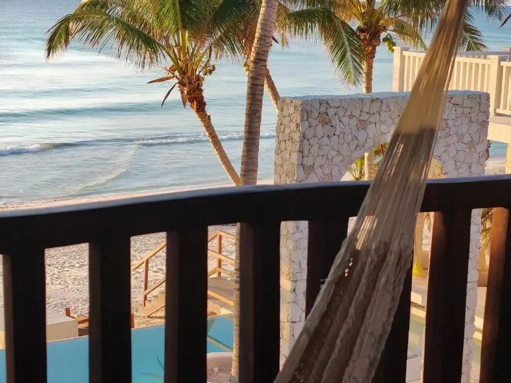 A hammock on a wooden balcony, with the palms and the sea.