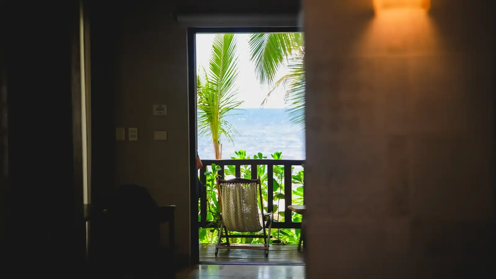 A dim passage opening onto a balcony with a chair and the sea beyond.