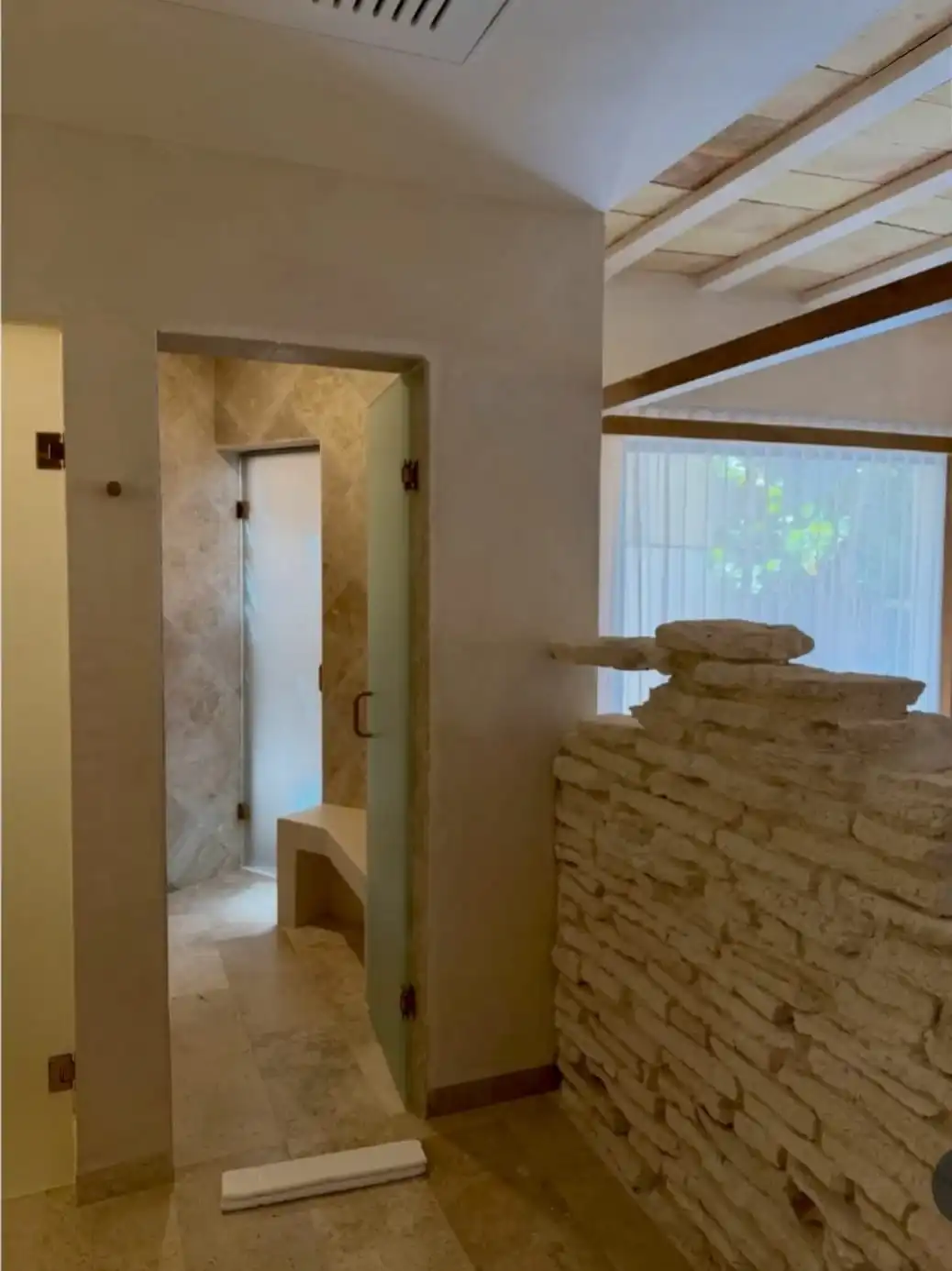 The way into the bathroom: a stacked-stone wall, a glass door and, behind it, the shower with its travertine bench.