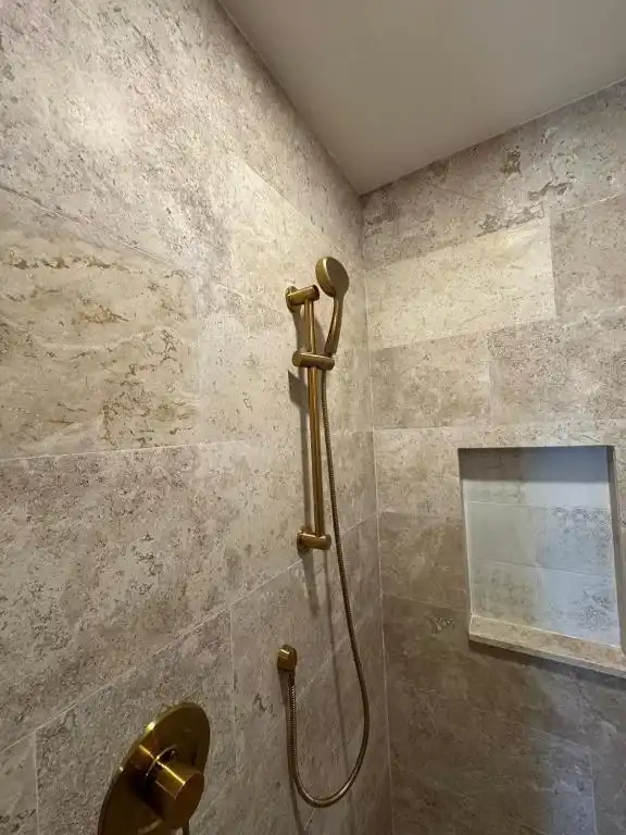A brass shower in a stone bathroom.
