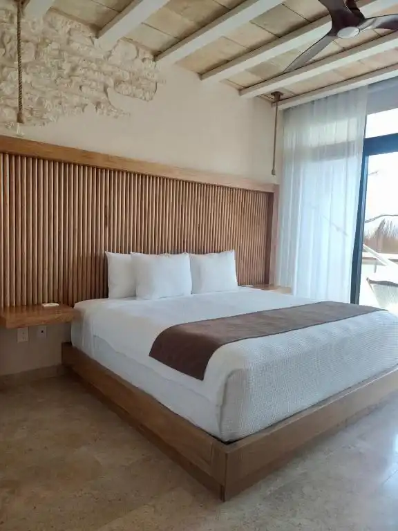 A bed with a slatted wooden headboard, under a beamed ceiling.