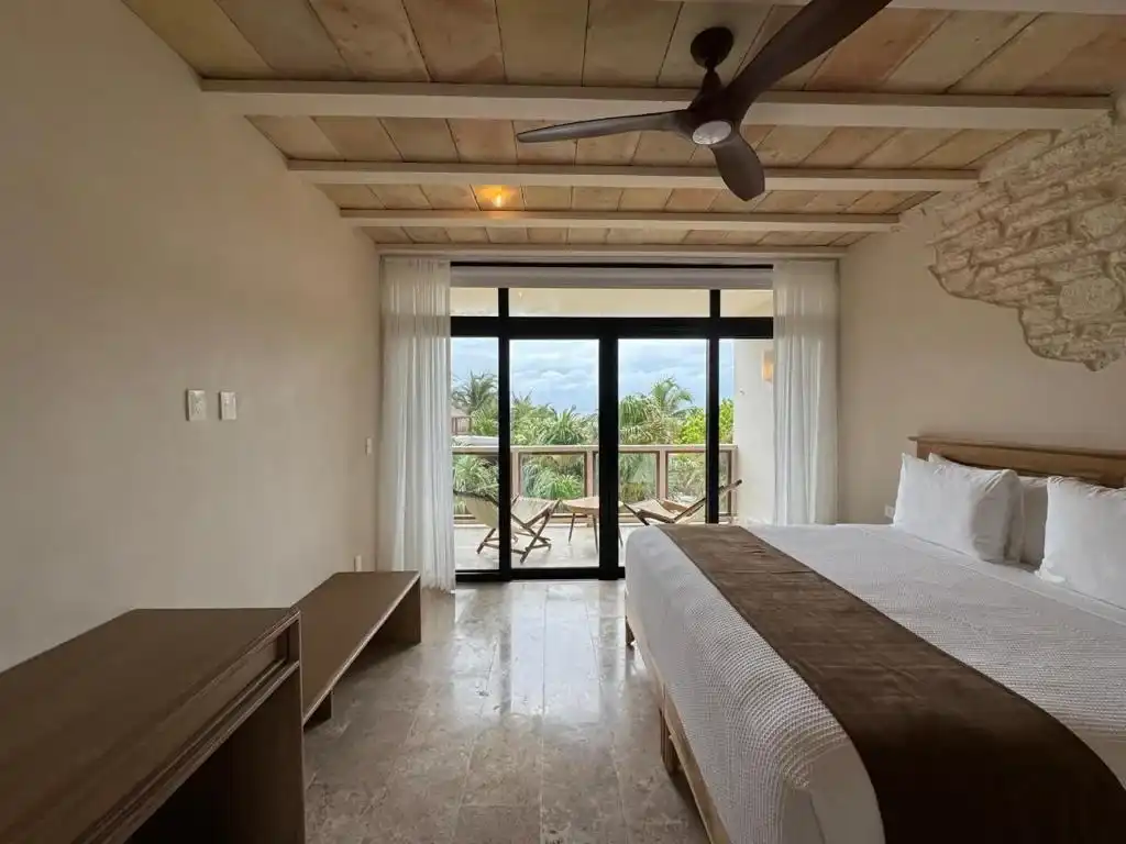 A room with a bed and a window wall, and a wooden bench at its foot.