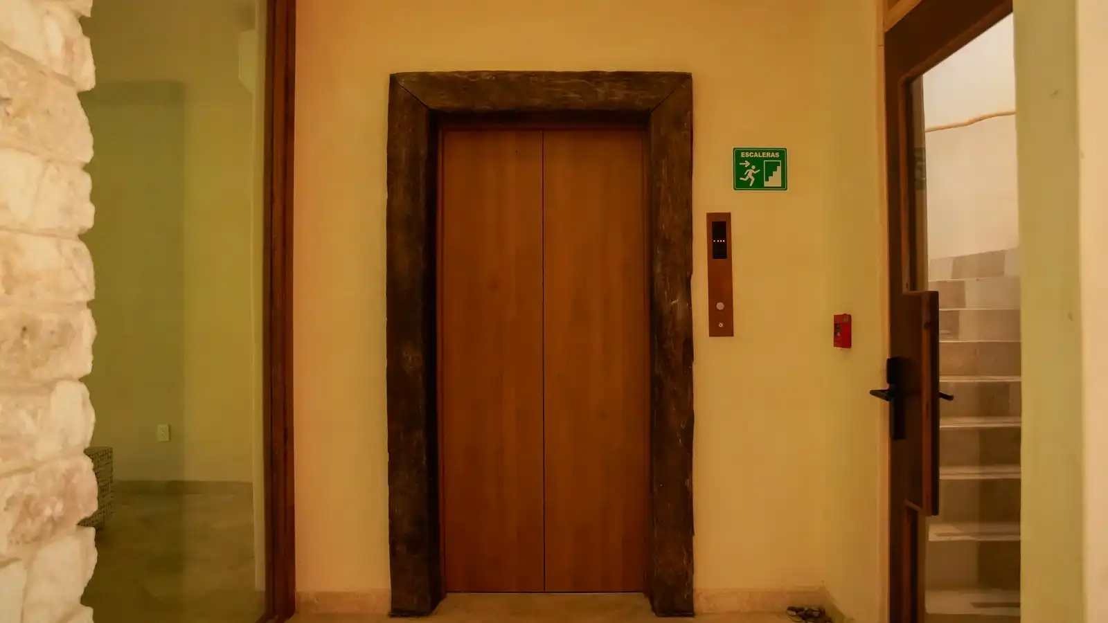 The hotel lift, with a wooden frame and the stairs signage beside it.