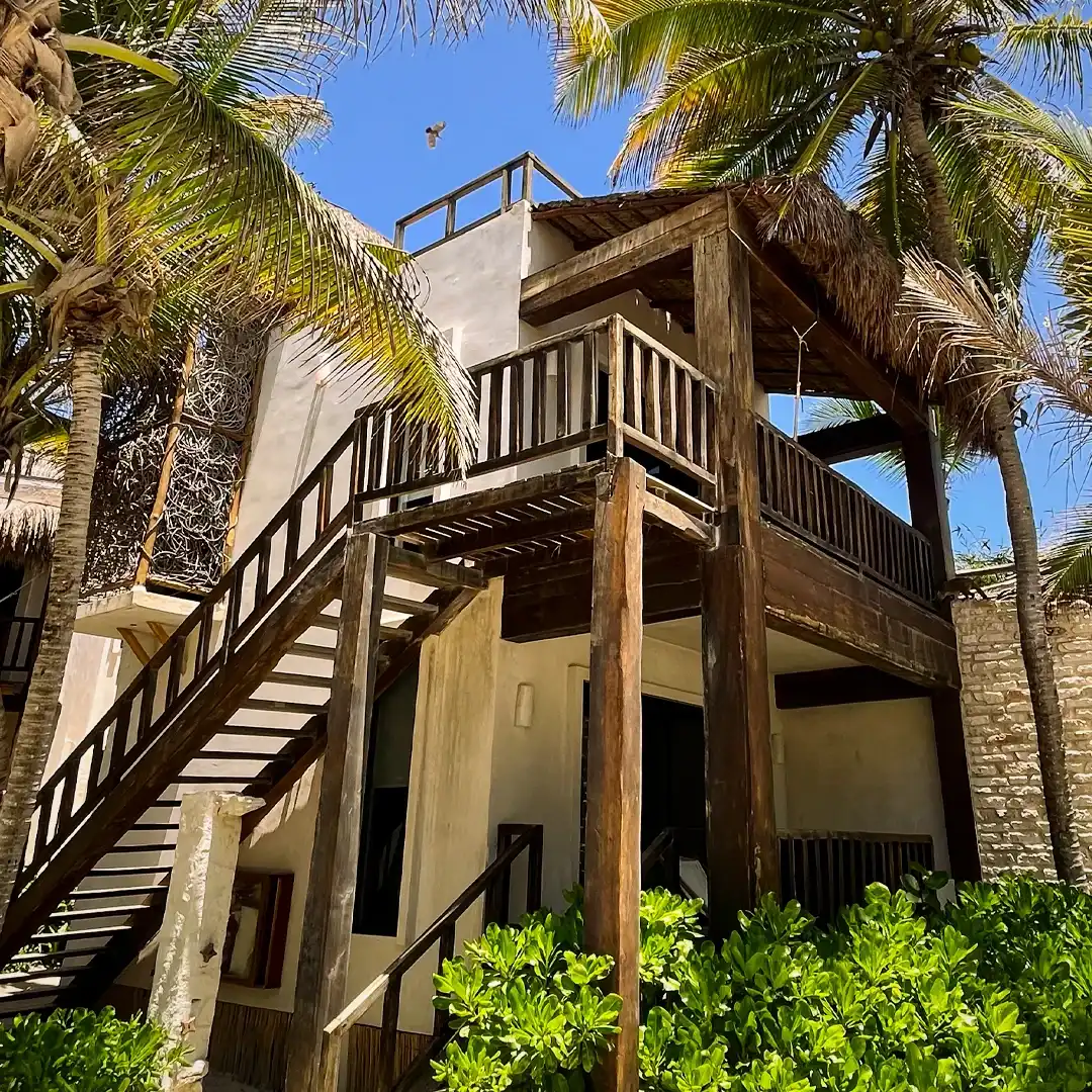 A hotel building with its wooden staircase and palm-thatched roof, among the palm trees.