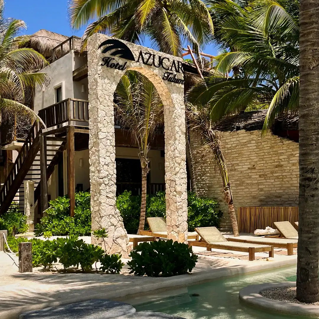 The stone arch with the hotel sign, the staircase and the loungers on the sand.
