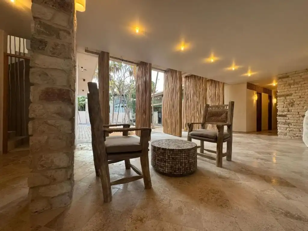 An interior lounge with wooden armchairs and a stone wall.