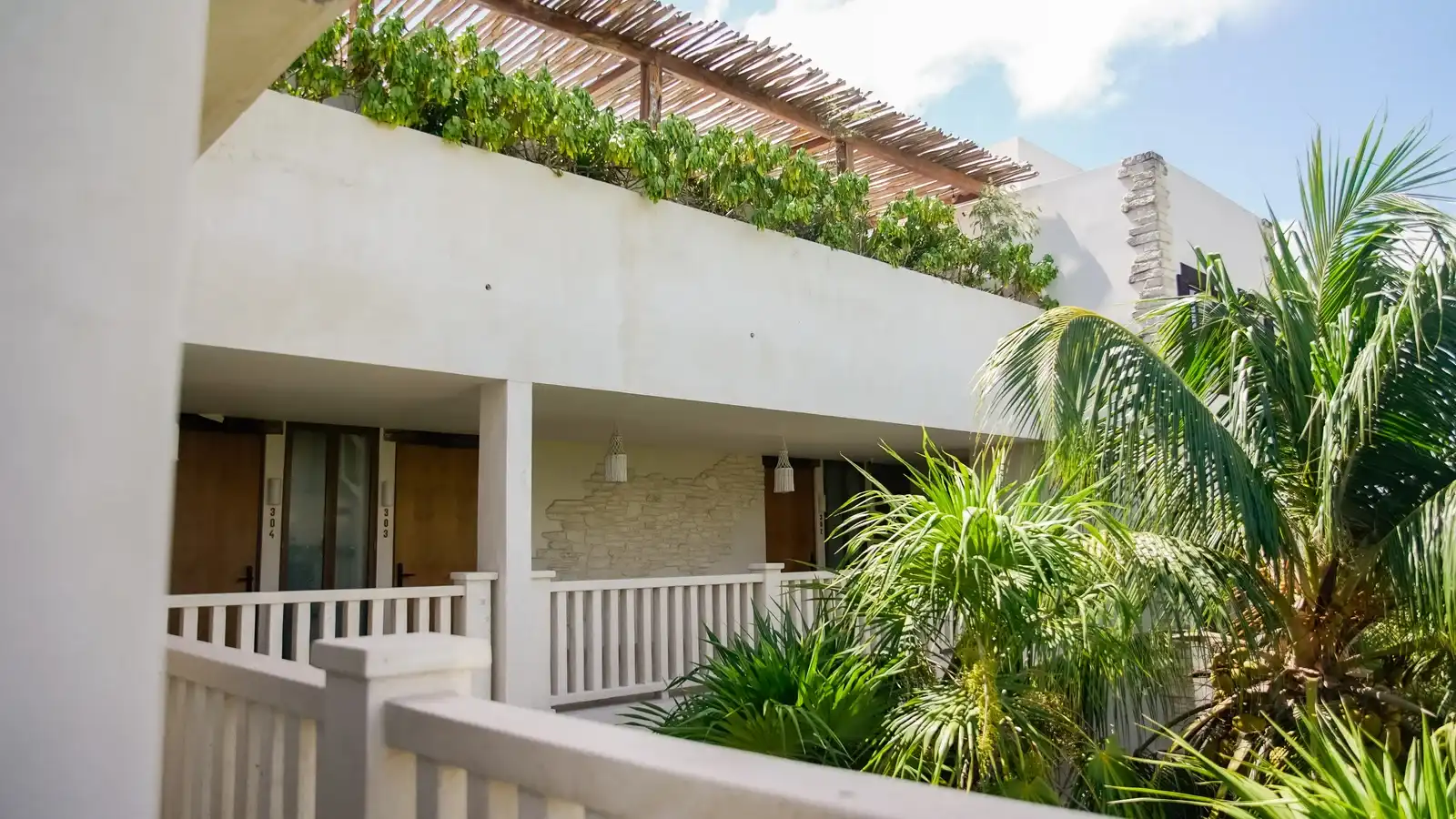 A white hotel building with its balconies, among the garden greenery.