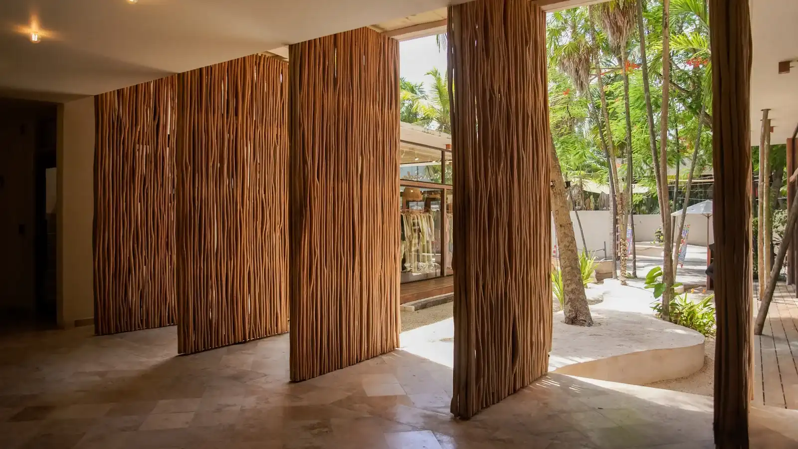 A passage lined with tree-trunk columns, open to the palm garden.