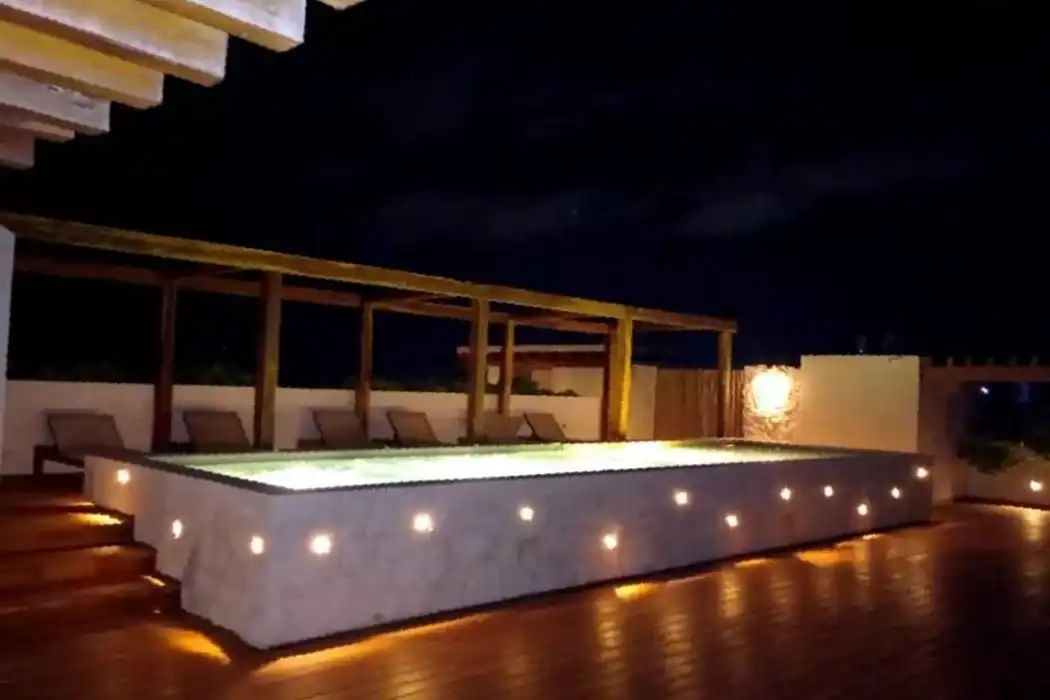 The rooftop pool at night, lit from within and by the lights set into its wall.